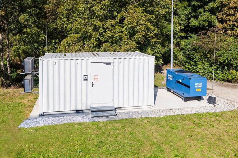 Steel generator enclosure installed on a concrete pad beside an acoustic canopy genset.