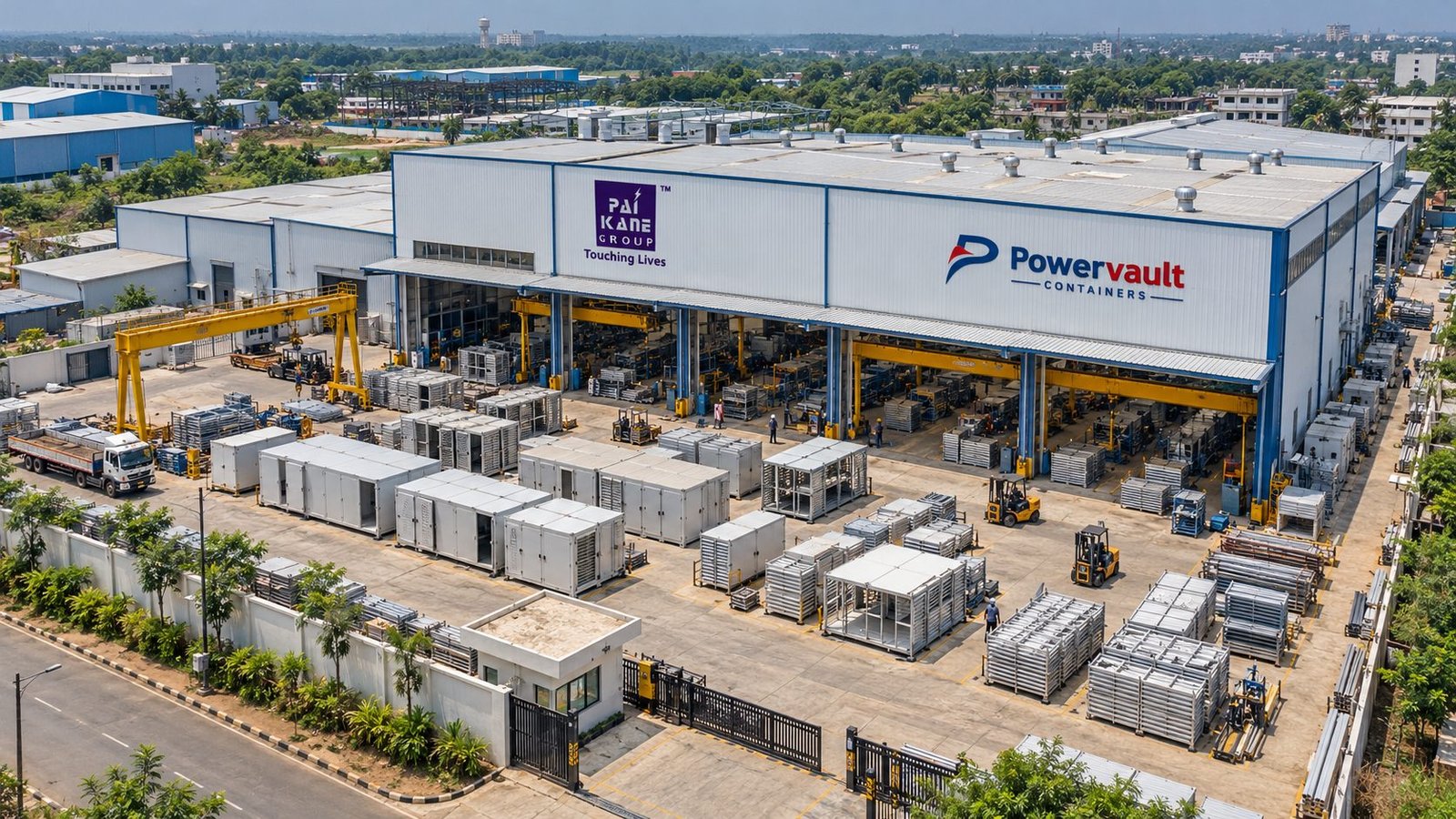 Aerial view of the Powervault Containers plant: a large fabrication hall with gantry cranes, forklifts and rows of steel enclosures and frames in the yard.